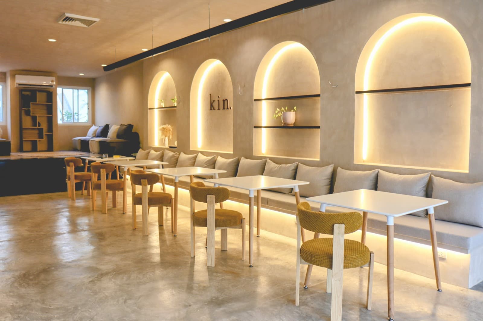 The Kin dining room: lit arches with shelves, a long banquette and mustard chairs