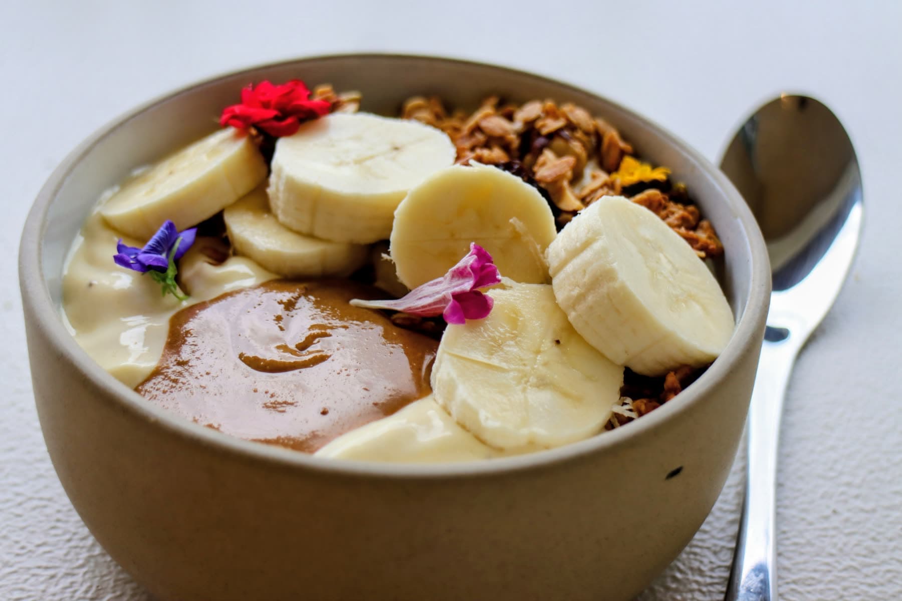 A breakfast bowl with banana, nut butter, granola and edible flowers