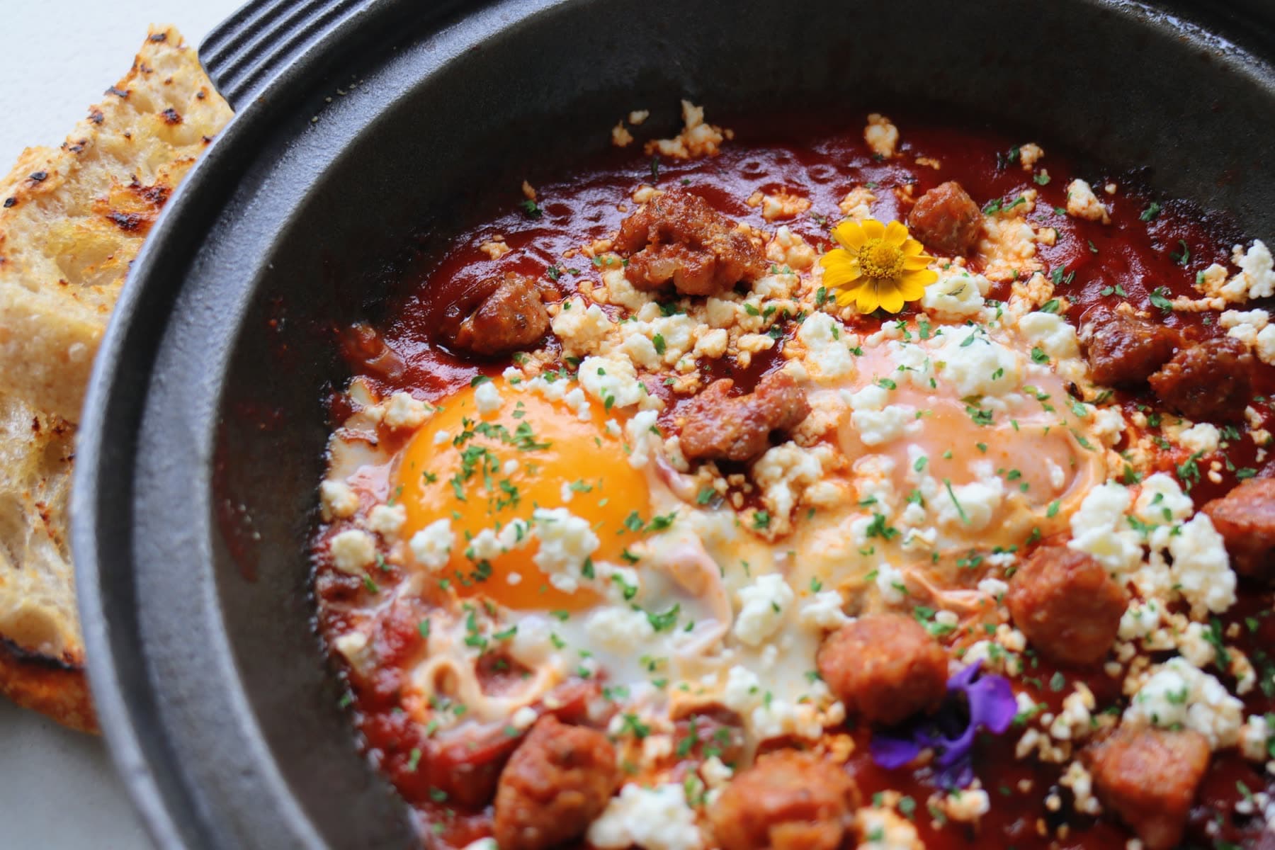 Chorizo shakshuka in a black pan with eggs, feta and grilled sourdough