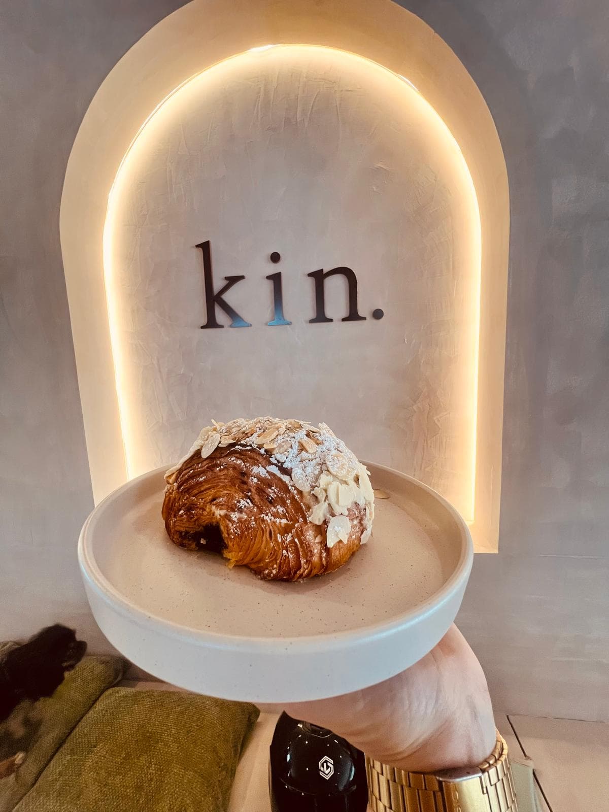 An almond croissant held up in front of the lit kin arch