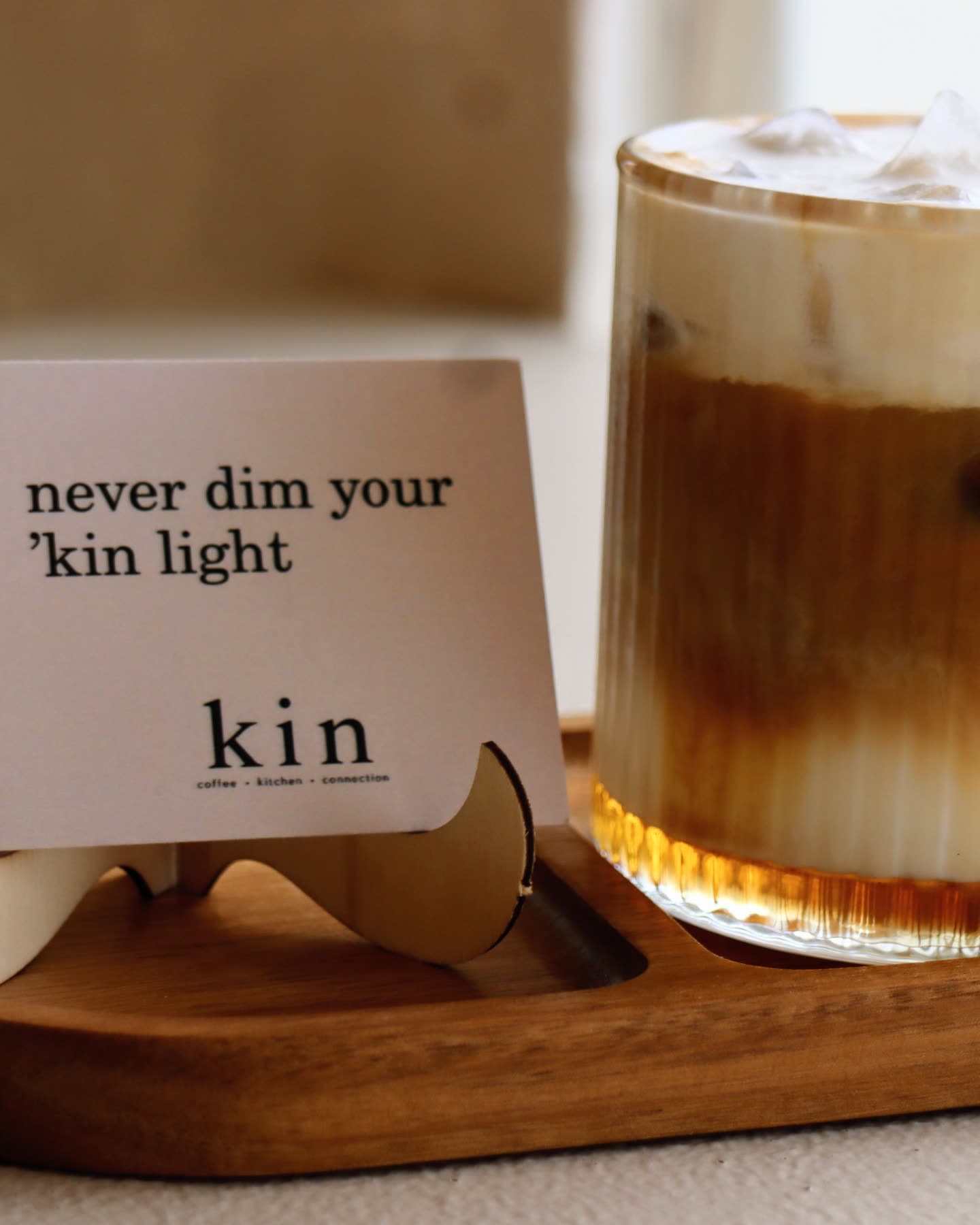 An iced latte on a timber tray, next to a kin card: never dim your 'kin light